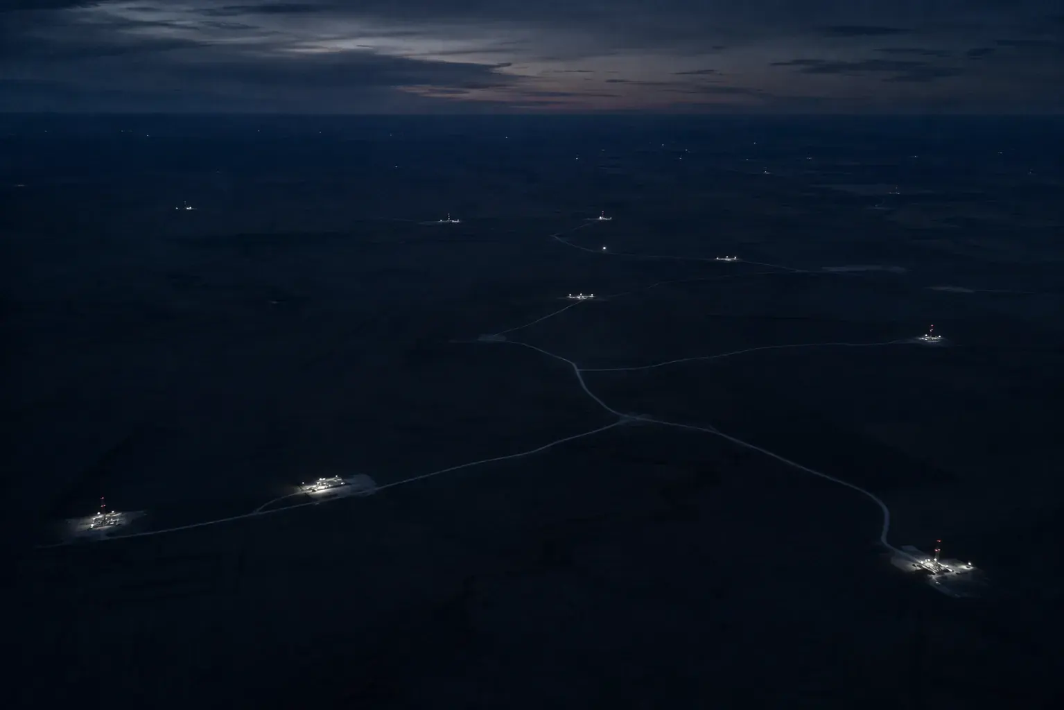 Aerial view of well sites and lease roads lit at dusk